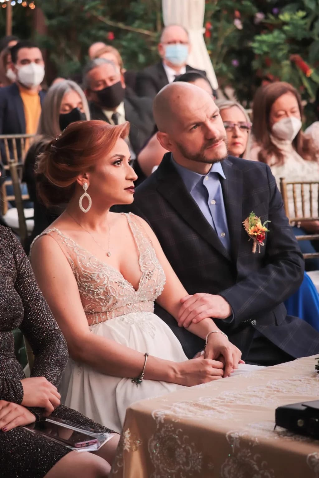 Florencia and Sean seated together at the signing table at their wedding, guests behind them under the trees