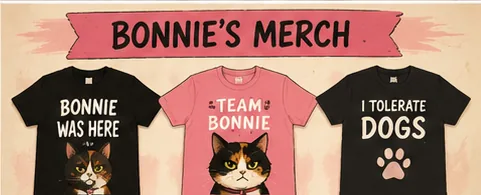 Under a painted banner reading BONNIE'S MERCH, three of Bonnie's imagined shirts hang in a row: BONNIE WAS HERE, TEAM BONNIE and I TOLERATE DOGS, each with a calico cat printed below the words