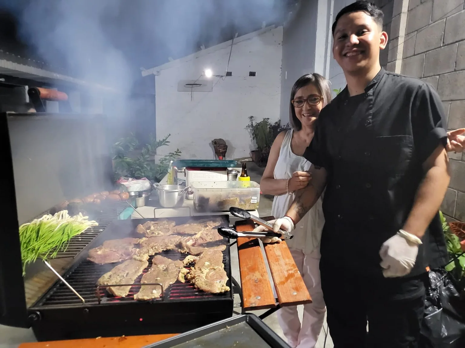 Florencia's mother and her brother Sigi at the grill, smoke rising off it between them