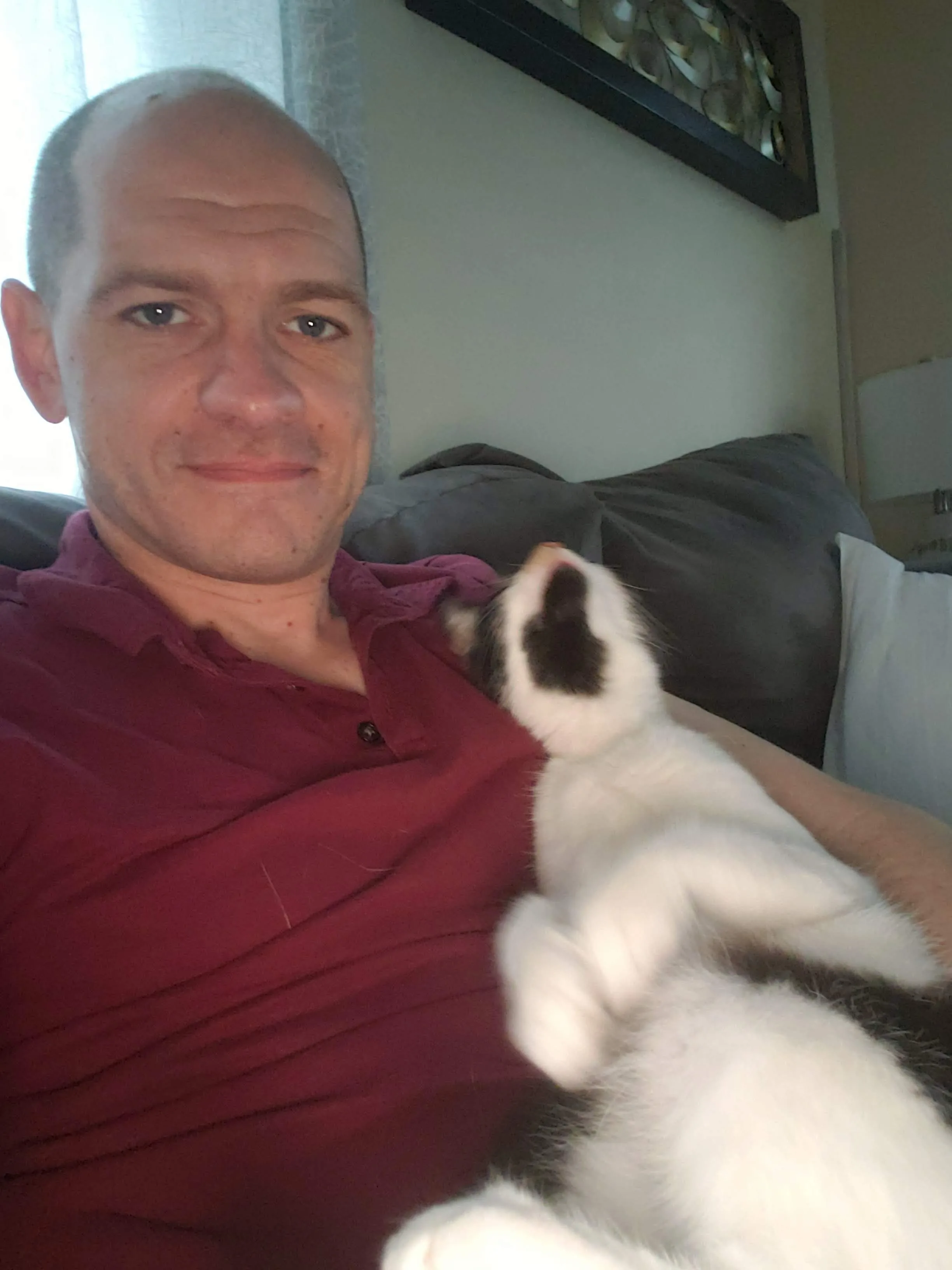 Sean in a dark red shirt holding kitten Bonnie up toward the camera, her white paws stretched out