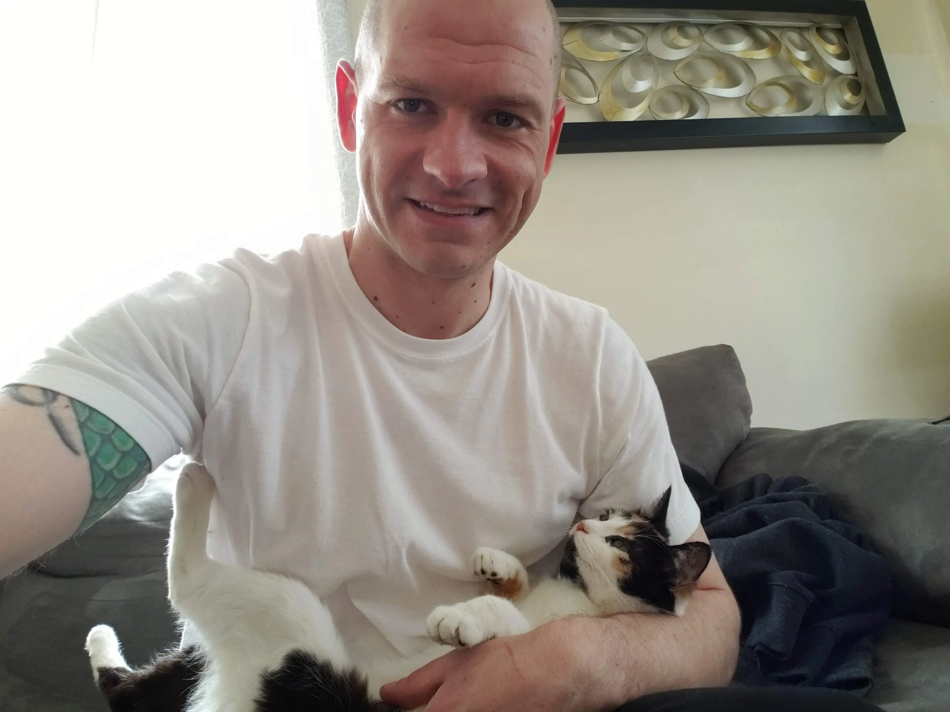 Sean on a grey sofa in a white t-shirt with Bonnie lying along his forearm, her paws up, both settled