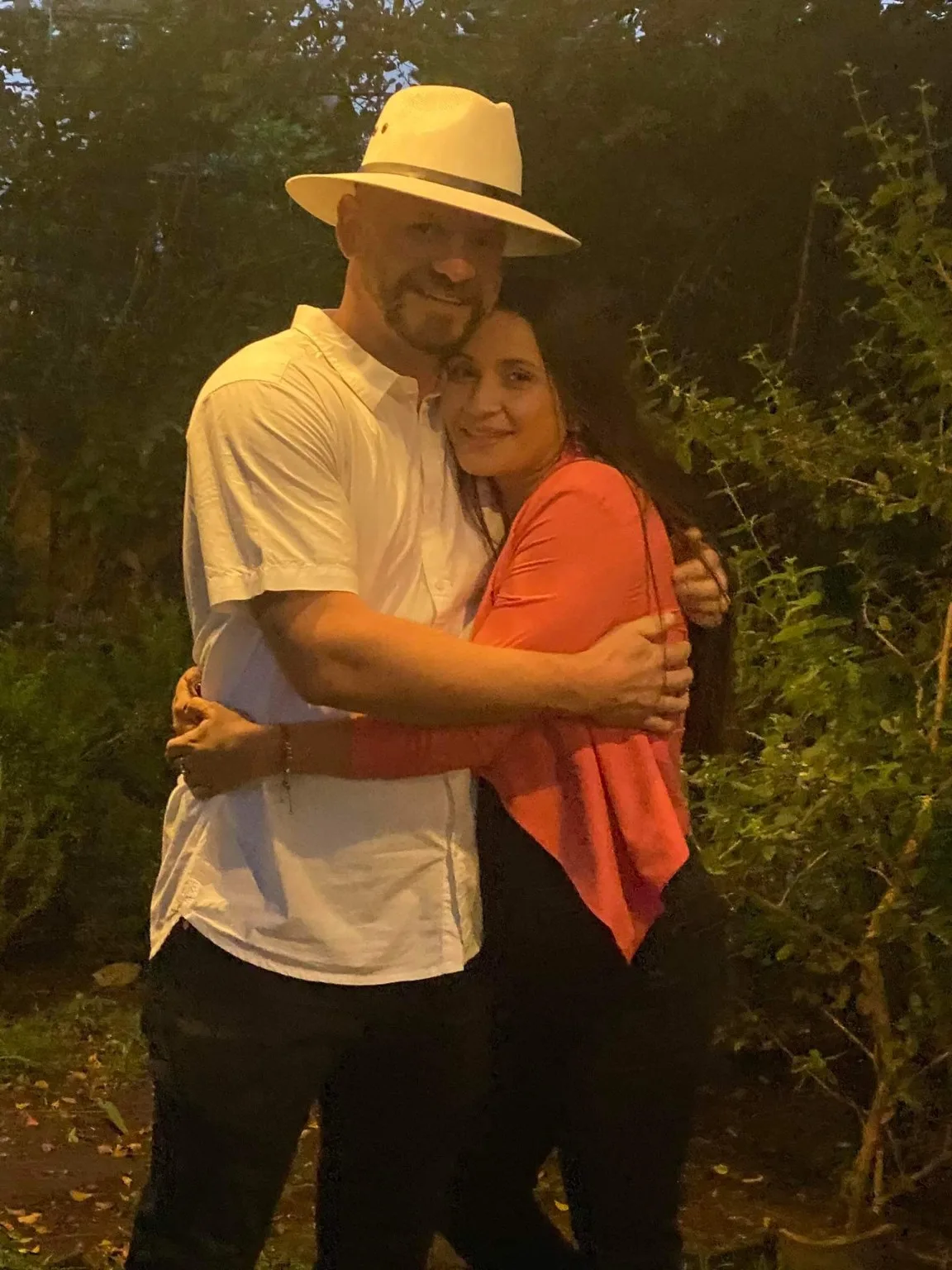 Florencia and Sean holding each other in the evening in El Salvador, greenery behind them